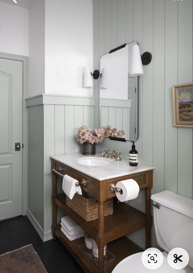 a white toilet sitting next to a sink in a bathroom under a mirror and light fixture