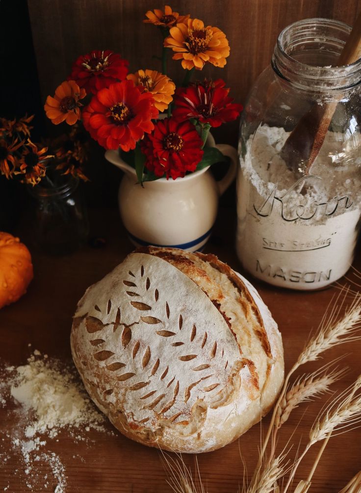 a loaf of bread sitting on top of a wooden table next to flowers and jars