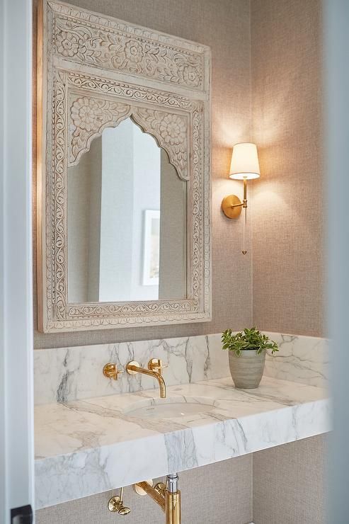 a bathroom with marble counter top and gold faucet, mirror above the sink