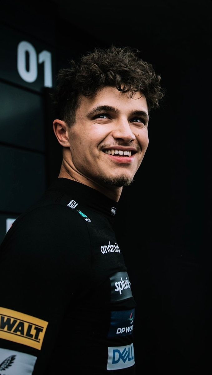 a smiling man in a black jersey standing next to a wall with numbers on it