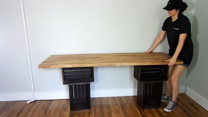 a woman in black shirt and hat standing next to a wooden table with drawers on it