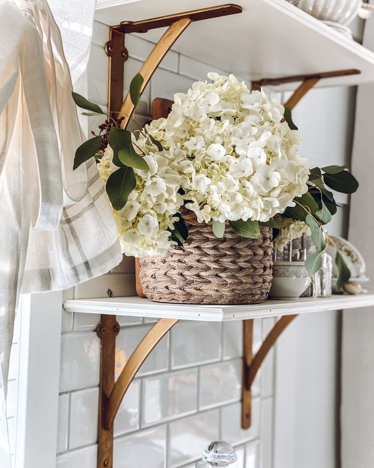 white flowers in a basket sitting on top of a shelf next to a towel rack