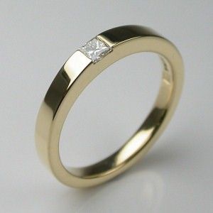 a yellow gold wedding ring with a princess cut diamond set in the center, on a white background