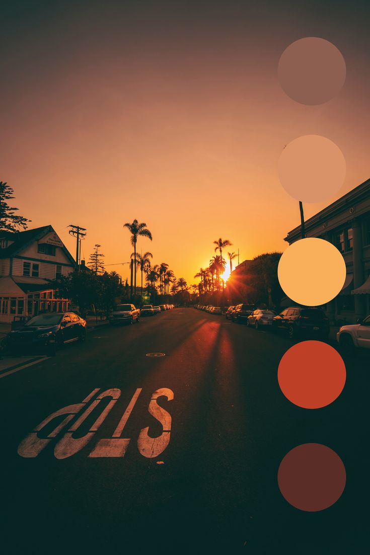 the sun is setting over an empty street with cars parked on both sides and palm trees in the background