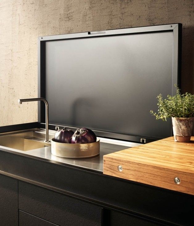 a kitchen sink with a wooden cutting board on the counter and a tv mounted above it