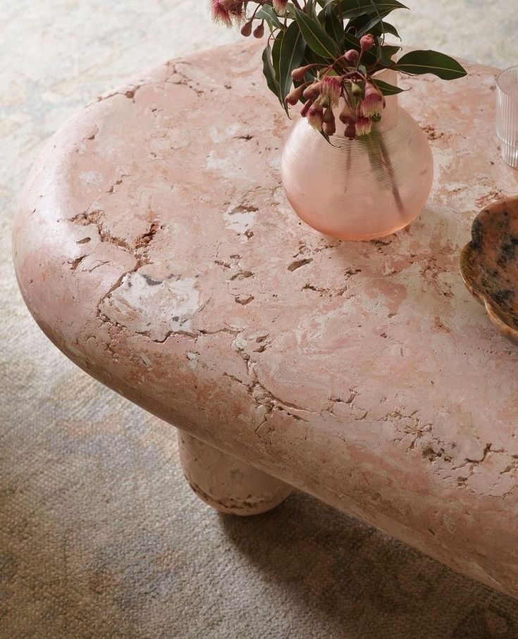 a vase with flowers sitting on top of a pink marble table next to a shell