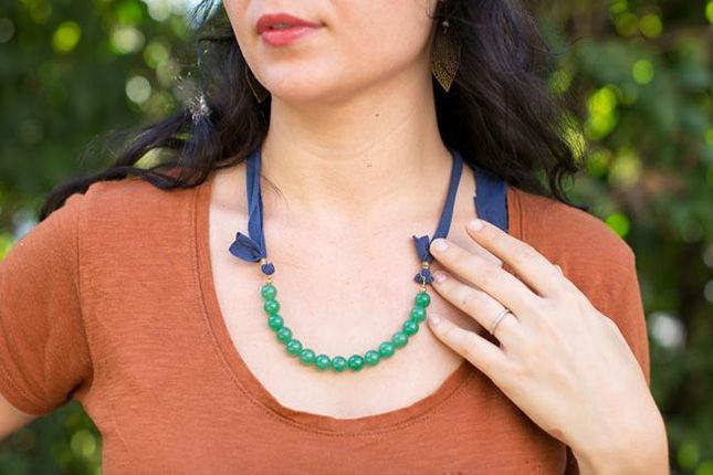 a woman wearing a green beaded necklace with blue ribbon around her neck and brown shirt