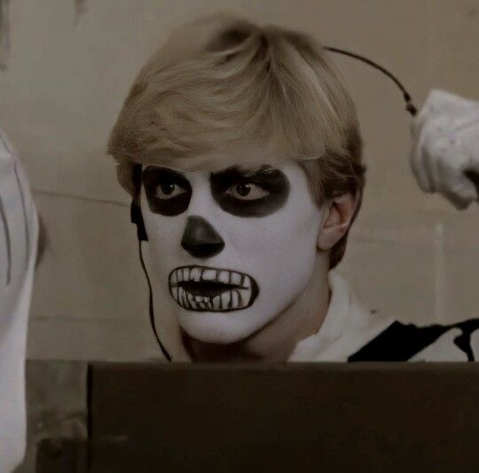 a man with white makeup and black face paint on his face is looking in the mirror