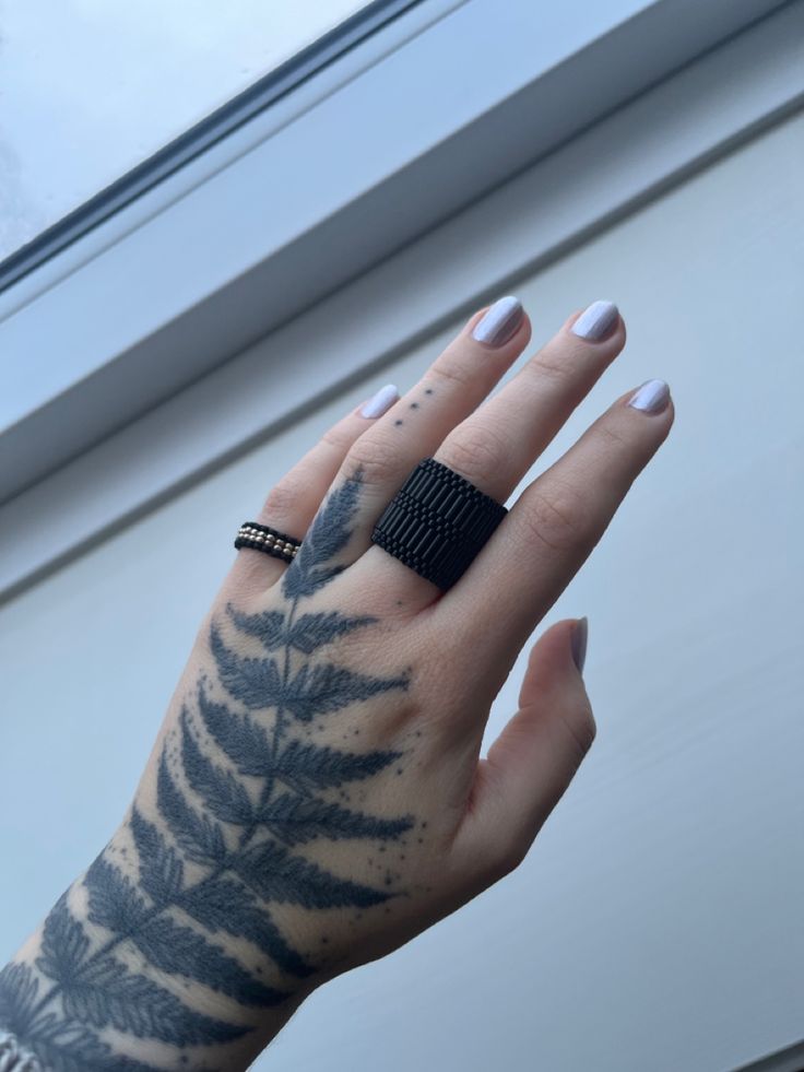 a woman's hand with tattoos on it and a ring in the middle of her finger