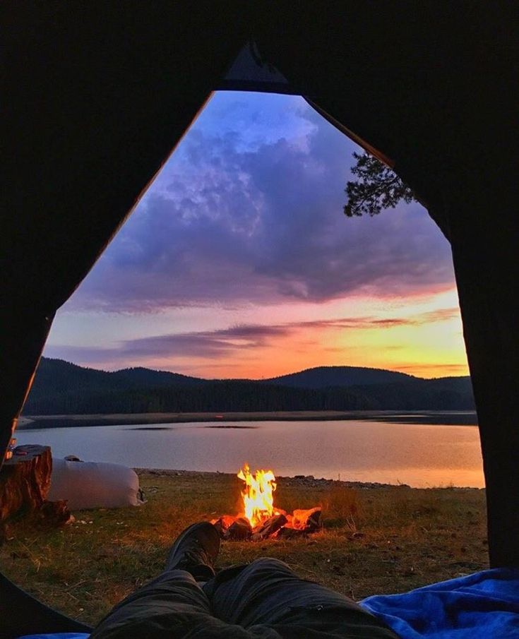 a person is sitting in front of a campfire at dusk with the sun setting