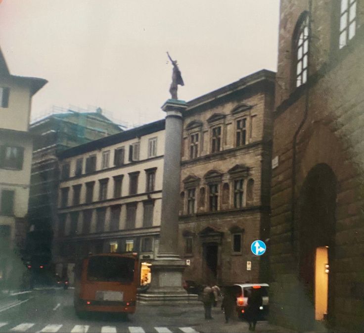 an old building with a statue in the middle and people walking on the sidewalk below