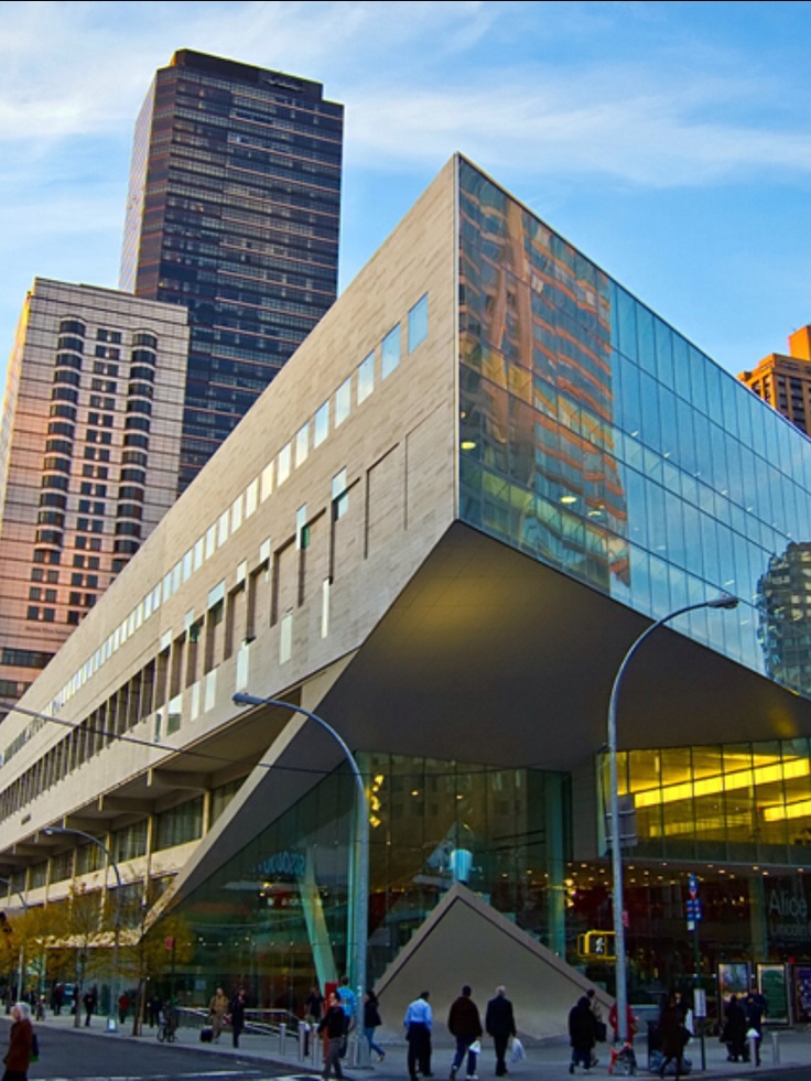 people are walking around in front of a building with many windows and glass on it