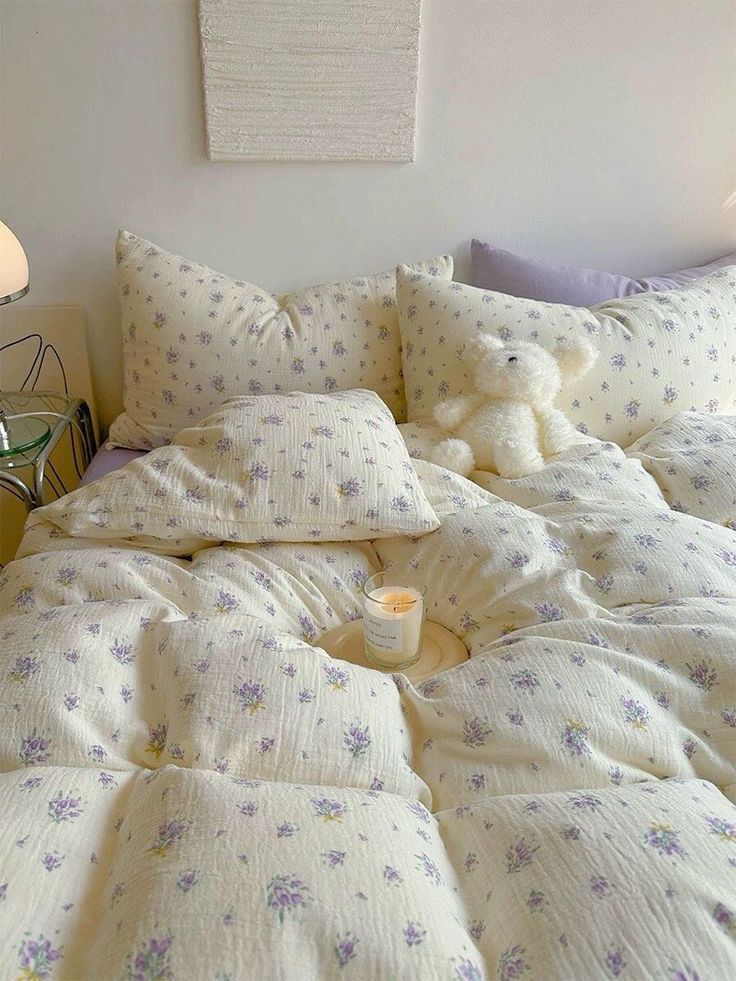 a teddy bear sitting on top of a bed with white sheets and purple floral pillows