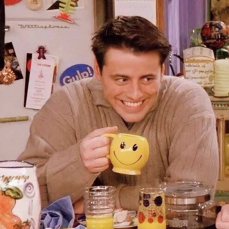 a man holding a yellow smiley face mug in front of a table with food on it