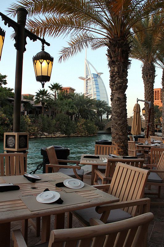 an outdoor dining area with palm trees and water in the background, along with tables and chairs