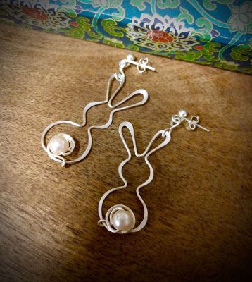 a pair of silver ear wires with white pearls hanging from them on a wooden surface