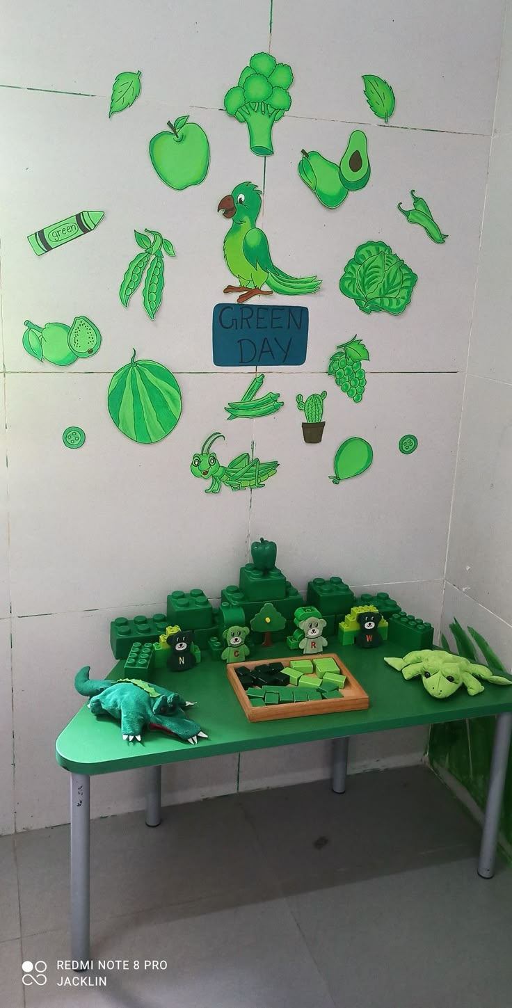 a green table topped with lots of cut out animals and plants next to a white wall