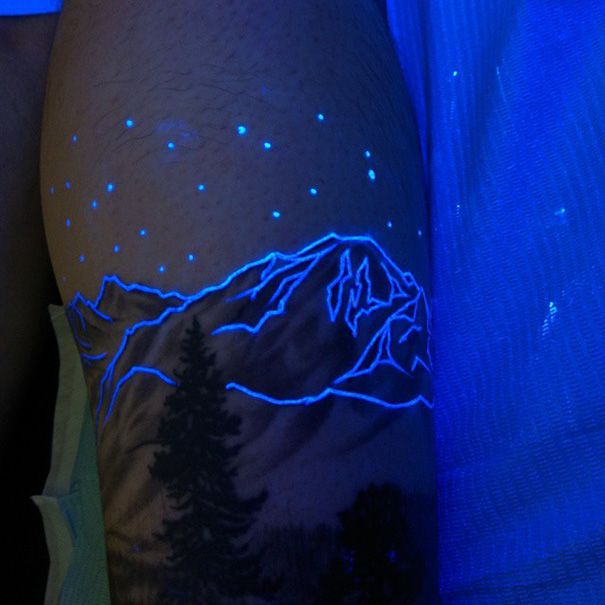 a man's arm with mountains and trees on it, under the glow of blue light