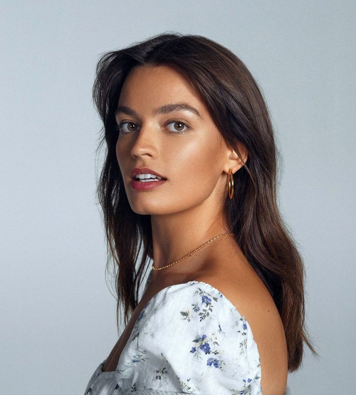 a woman with long hair wearing a white top and gold earrings is posing for the camera