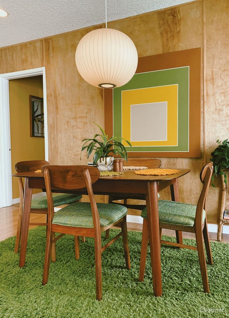 a dining room table and chairs with green rugs on the floor in front of it