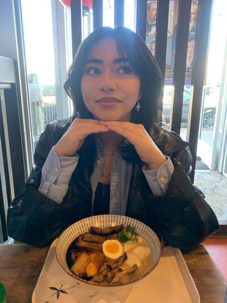 a woman sitting at a table in front of a bowl of food with an egg on it