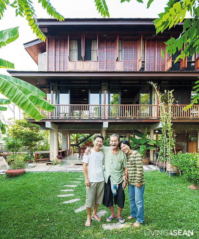 three people standing in front of a large building with trees and plants around it, posing for the camera