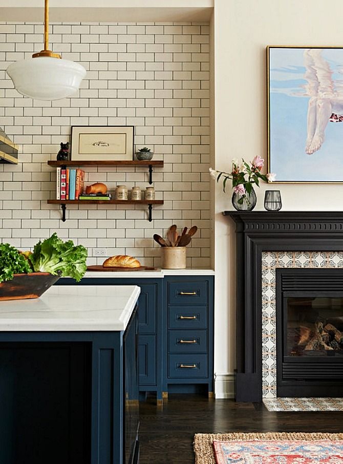 a kitchen with blue cabinets and a white brick fireplace in the center, along with an art work on the wall