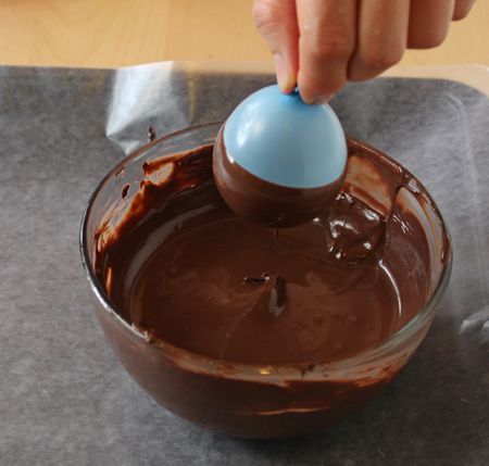 a person is mixing chocolate in a bowl with a blue plastic egg on the top