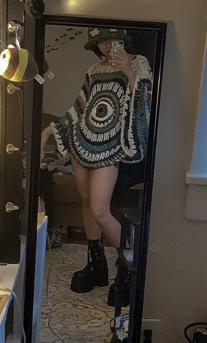 a woman standing in front of a mirror wearing boots and a crocheted sweater