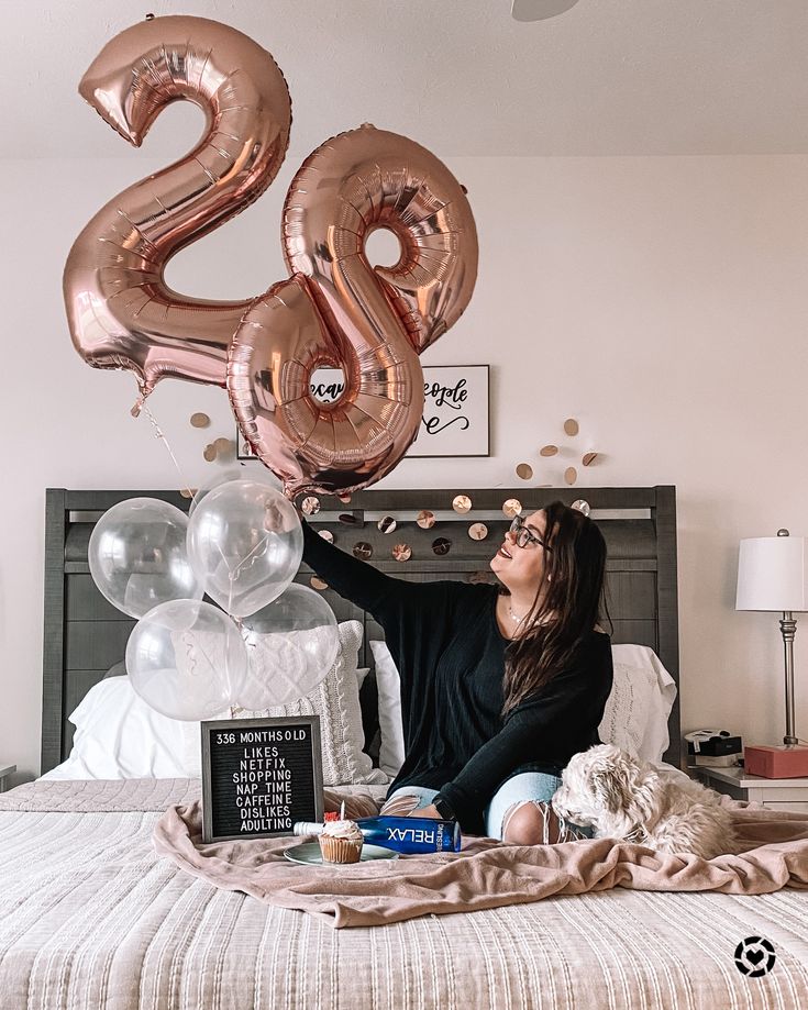 a woman sitting on top of a bed with balloons in the shape of two numbers