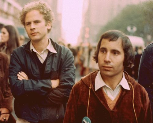 two men standing next to each other in front of a group of people on a city street