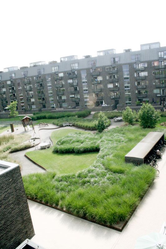 an open courtyard with benches and grass in the center, surrounded by apartment buildings on either side