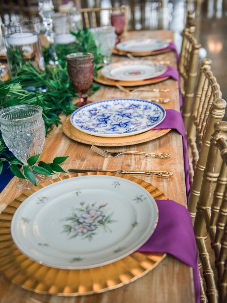 the table is set with blue and white plates, gold rimmed dishes, and purple napkins