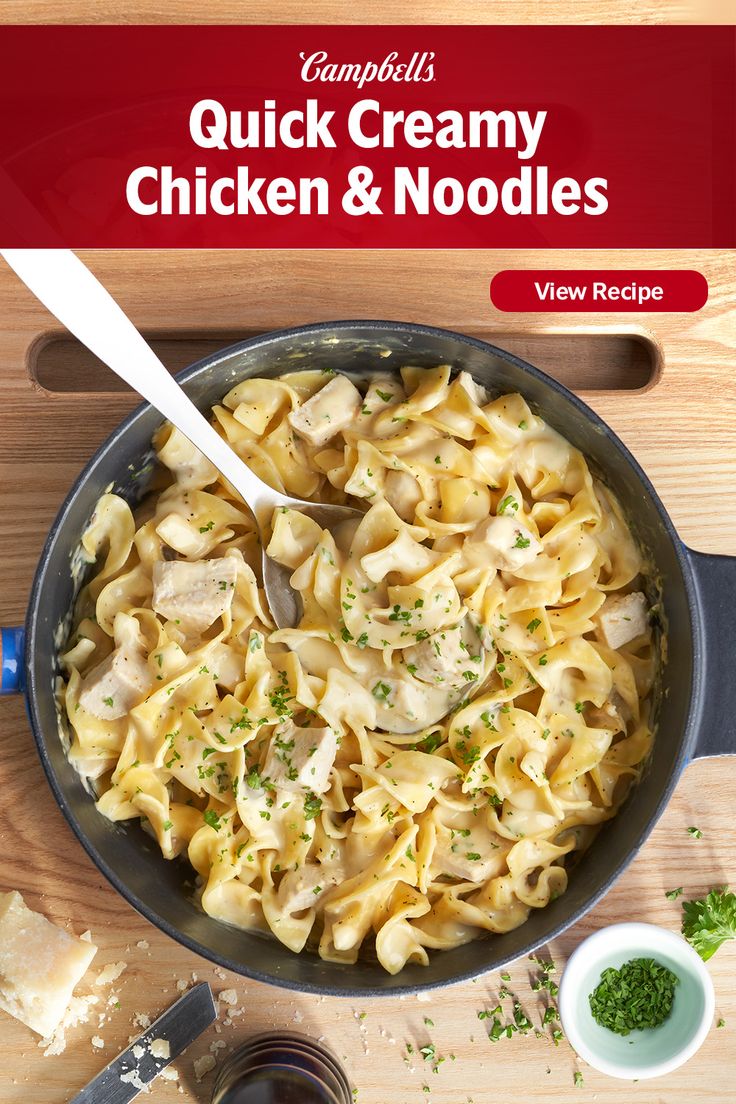 a skillet filled with chicken and noodles on top of a wooden table next to garlic