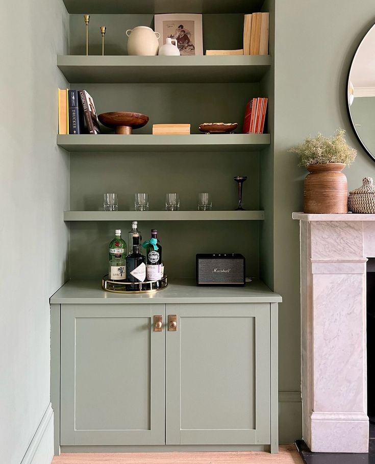 there is a shelf with bottles and glasses on it next to a fire place in the living room