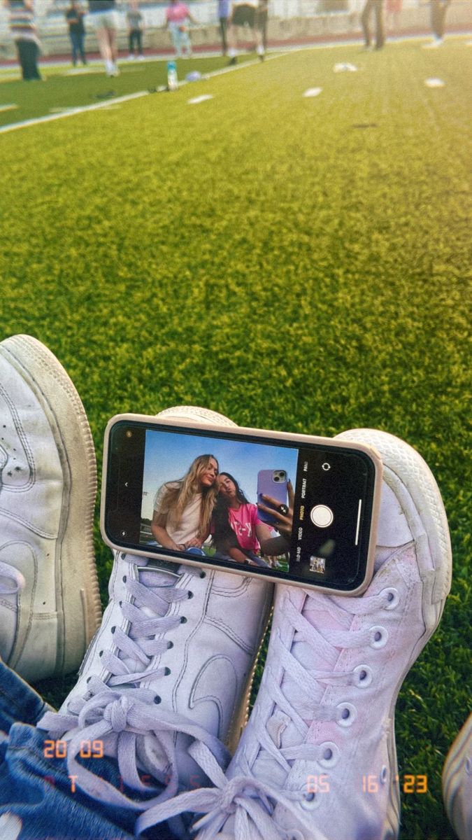 someone is taking a photo with their cell phone while sitting on the grass in front of a soccer field