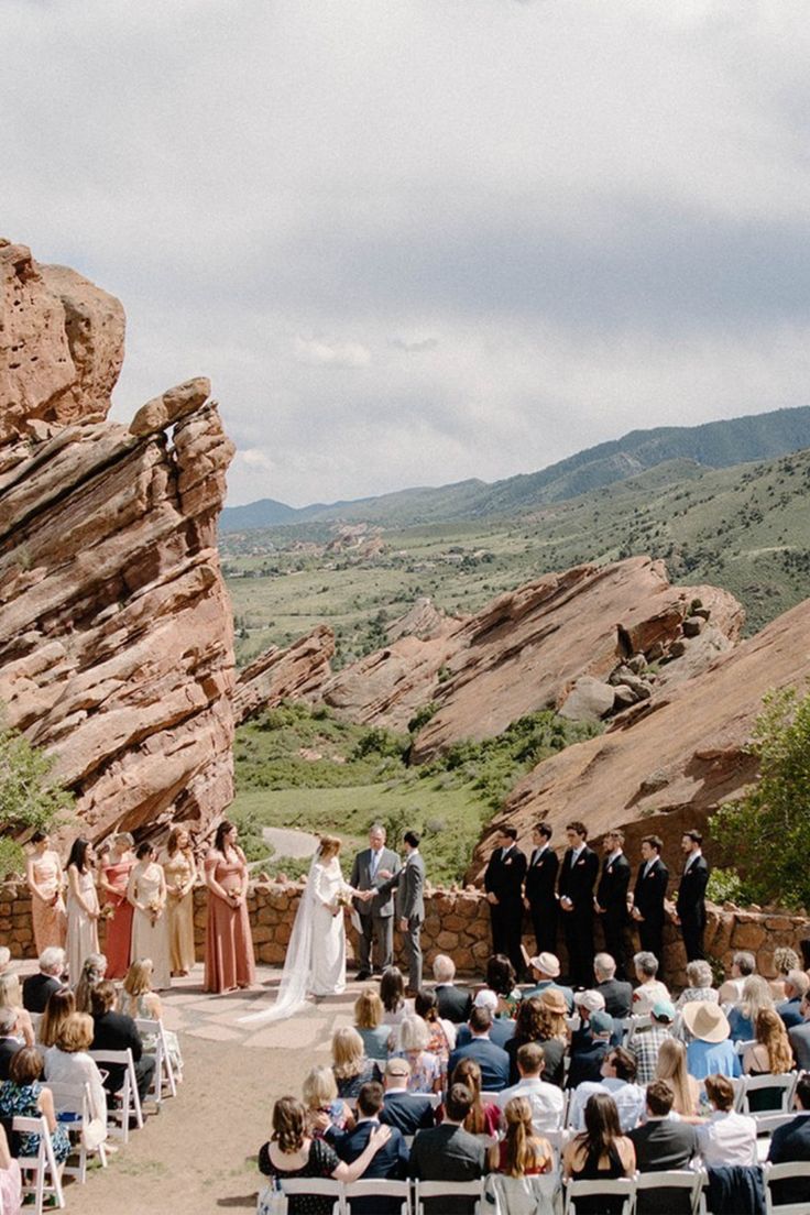 a wedding ceremony in the mountains with people sitting on chairs and looking at each other