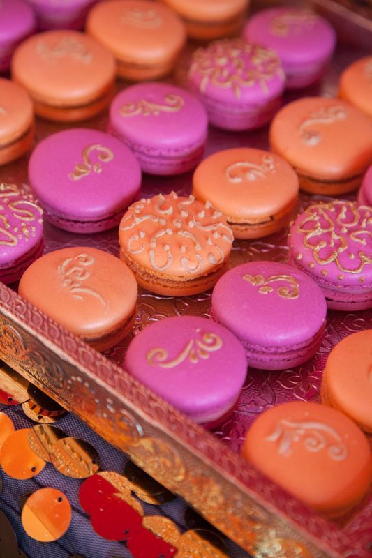 colorful macaroons are on display in a gold and pink box with ornate designs