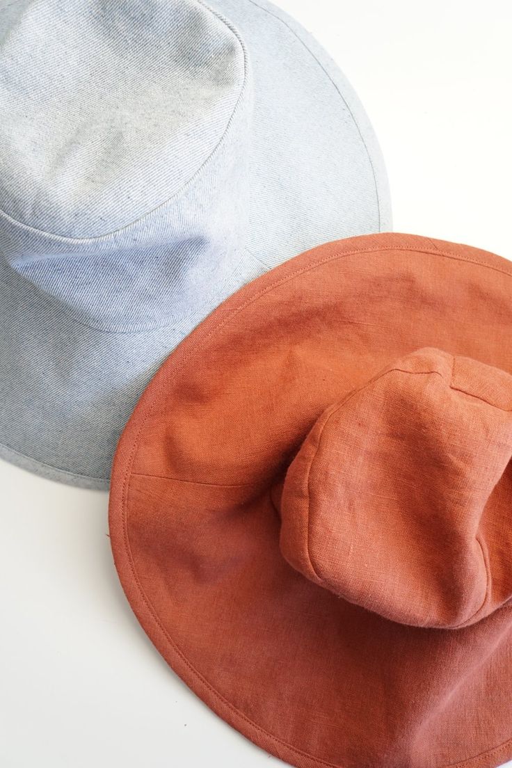 two hats sitting next to each other on top of a white table with an orange and gray hat