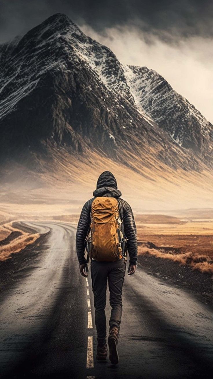 a man with a backpack walking down the middle of a road in front of a mountain