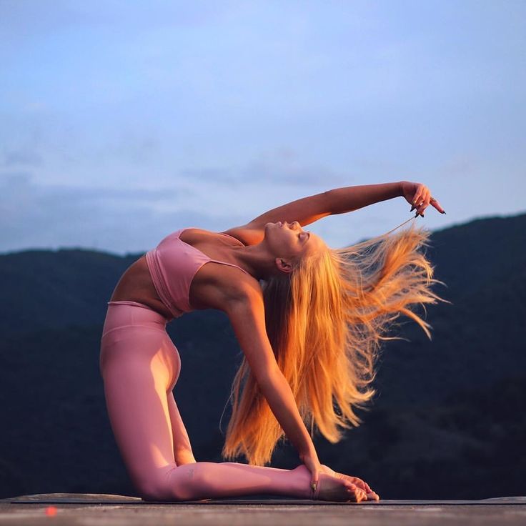 a woman with long blonde hair is doing yoga on the ground in front of mountains