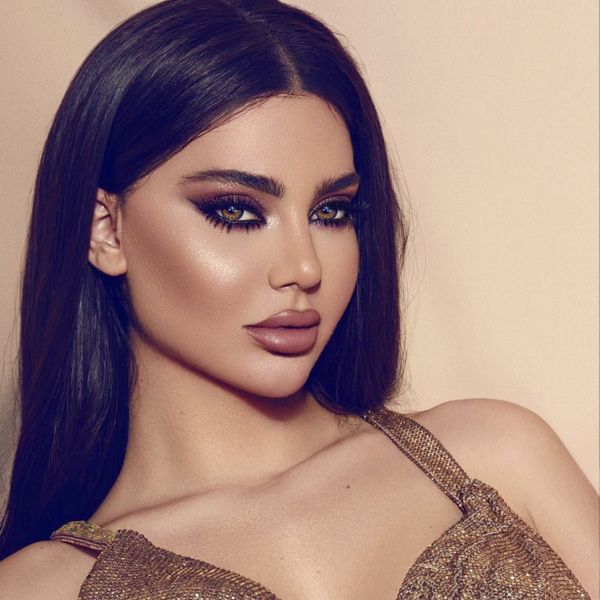 a close up of a woman with dark hair and makeup wearing a gold dress looking at the camera