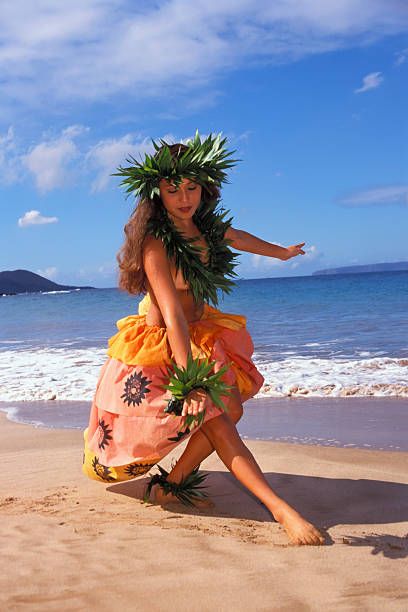 a woman in an orange dress on the beach with a hula skirt and flower wreath around her neck