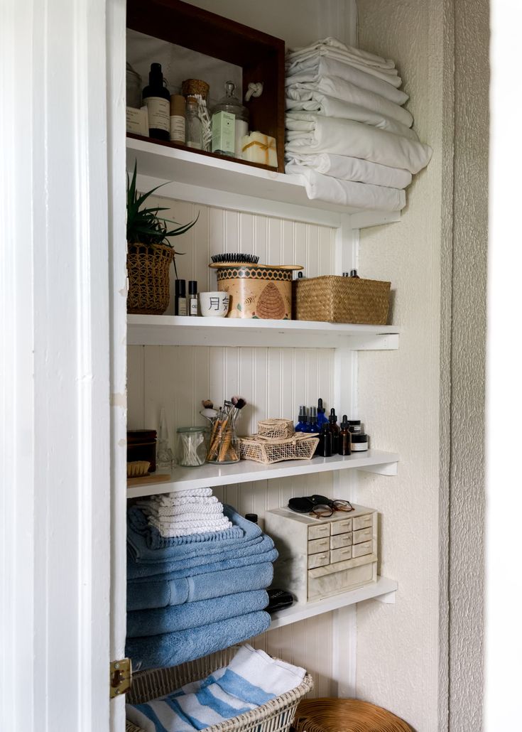 a bathroom with shelves filled with towels and other items on it's sides, next to a basket full of toiletries