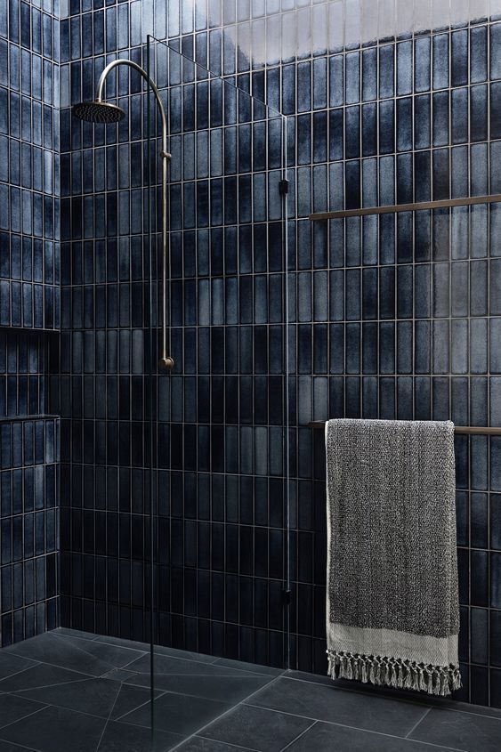 a black tiled bathroom with a towel hanging on the shower head and hand rail in front of it