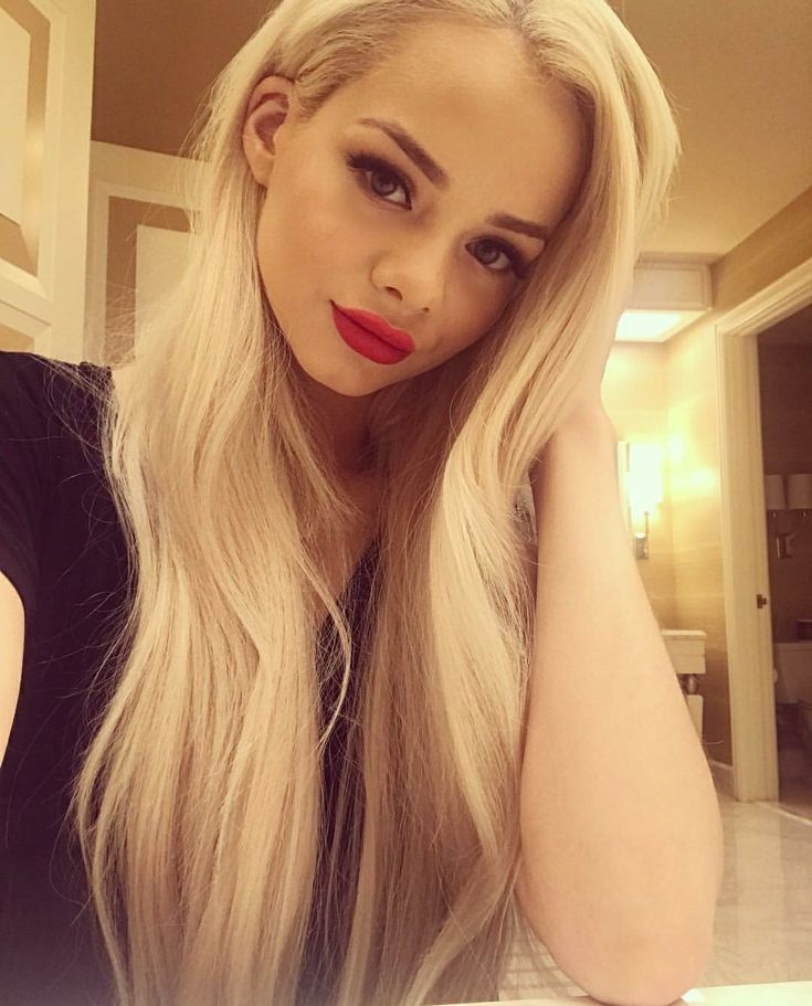 a woman with long blonde hair and red lipstick posing for a photo in front of a mirror