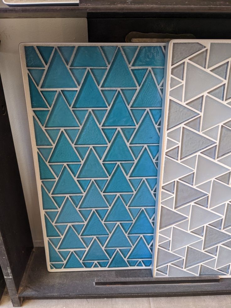 two decorative tiles sitting next to each other on top of a shelf in a room