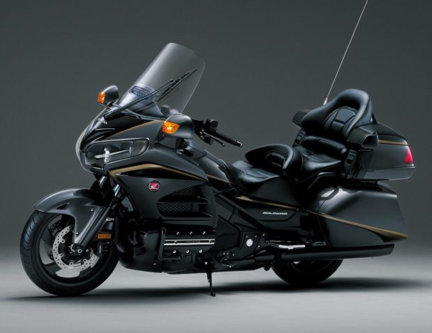 a black and gold motorcycle is parked on a gray background with its lights on,