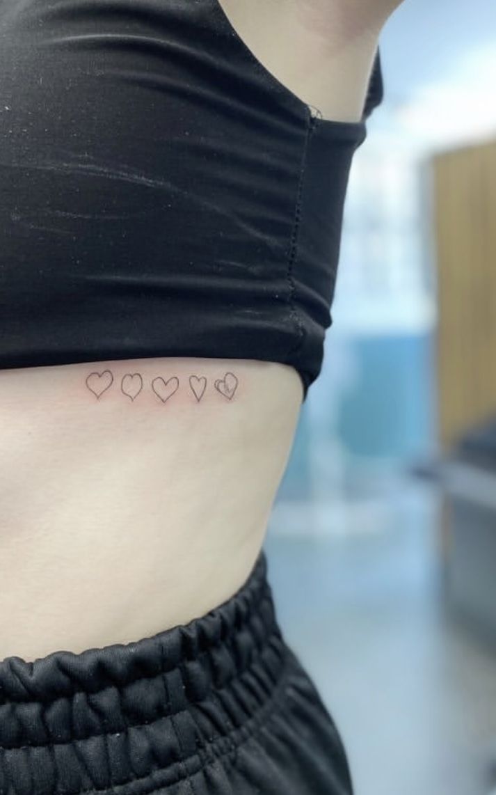 a woman's stomach with small hearts on the lower part of her belly and behind her is a black tank top