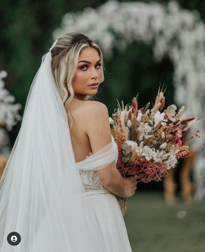 a woman in a wedding dress holding a bouquet of flowers and wearing a long veil